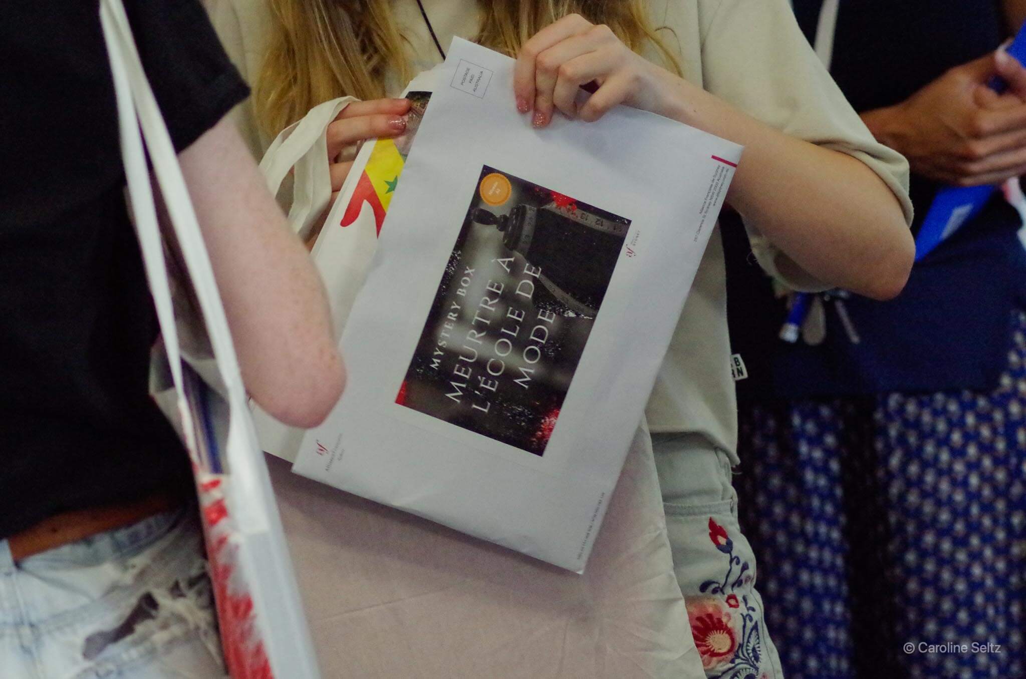 Student holds an envelope containing a Mystery Box whodunit game by Alliance Francaise de Sydney. 